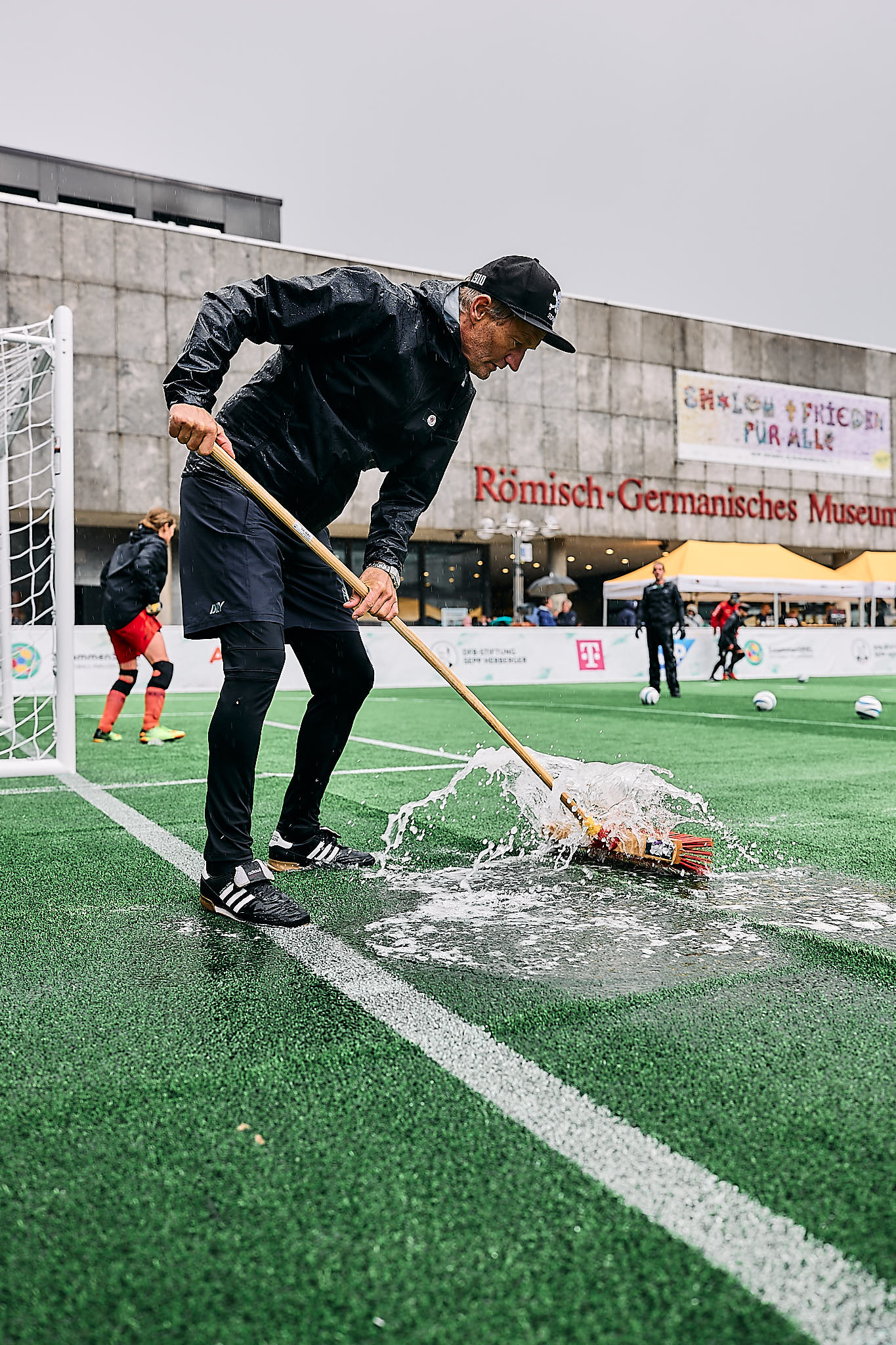 Besen in die Hand und weg mit dem Wasser - auch Coach Wolf Schmidt sorgte dafür, dass beide Teams nach dem Gewitter auf einem möglichst wenig von Wasser bedeckten Kunstrasen spielen konnten.